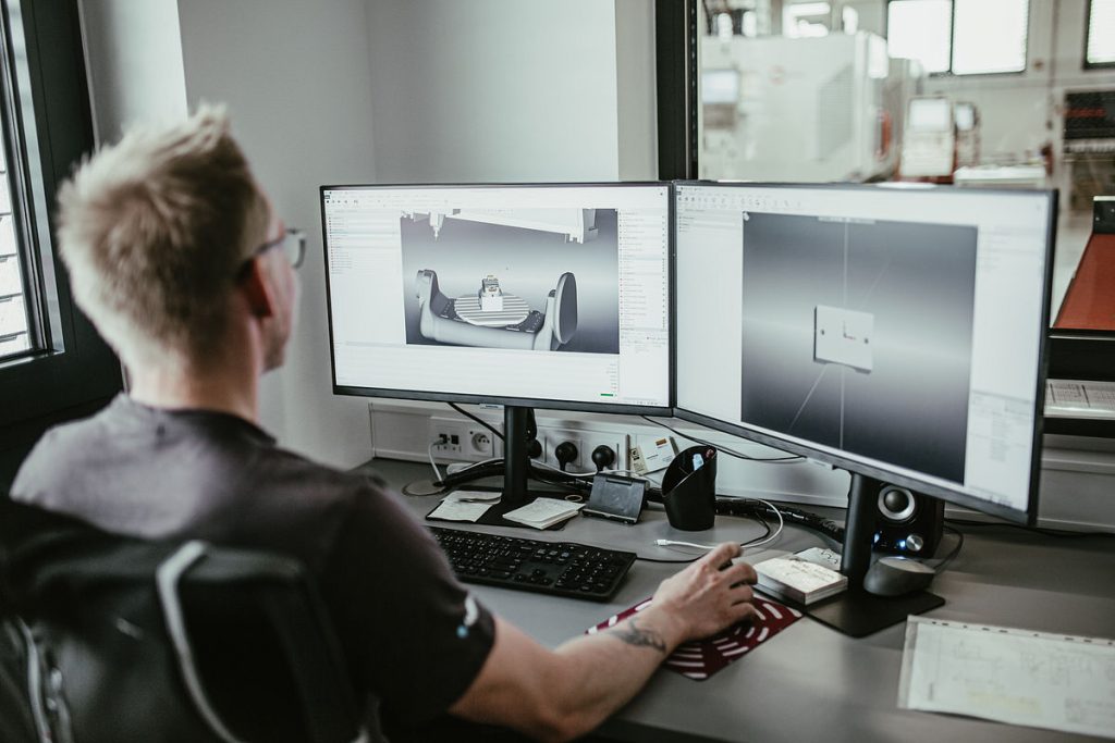 An RF SPIN engineer programming a machining job in GibbsCAM on two monitors