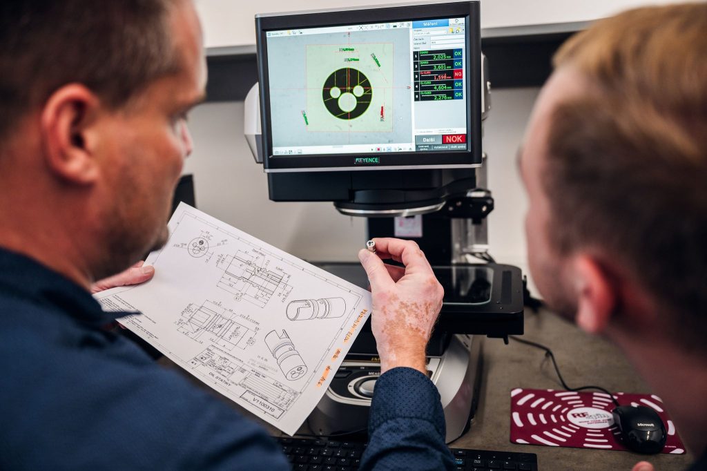 An engineer checks a machined part against its drawing on an optical measuring microscope